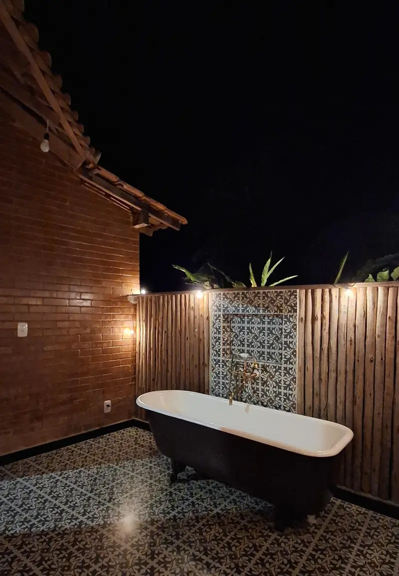 Banheira vitoriana da Cabana Estrela entre paredes de tijolo ecológico e ladrilhos decorados, a céu aberto, iluminada à noite