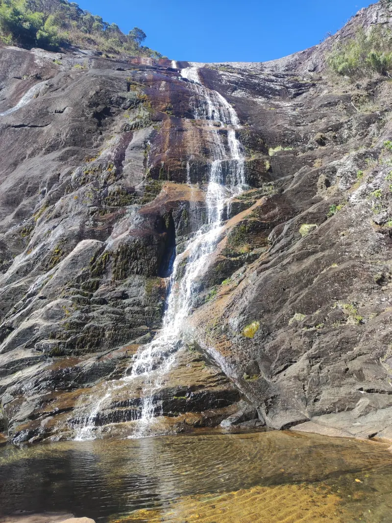 Cachoeira estreita descendo por paredão de rocha em meio à mata do Caparaó