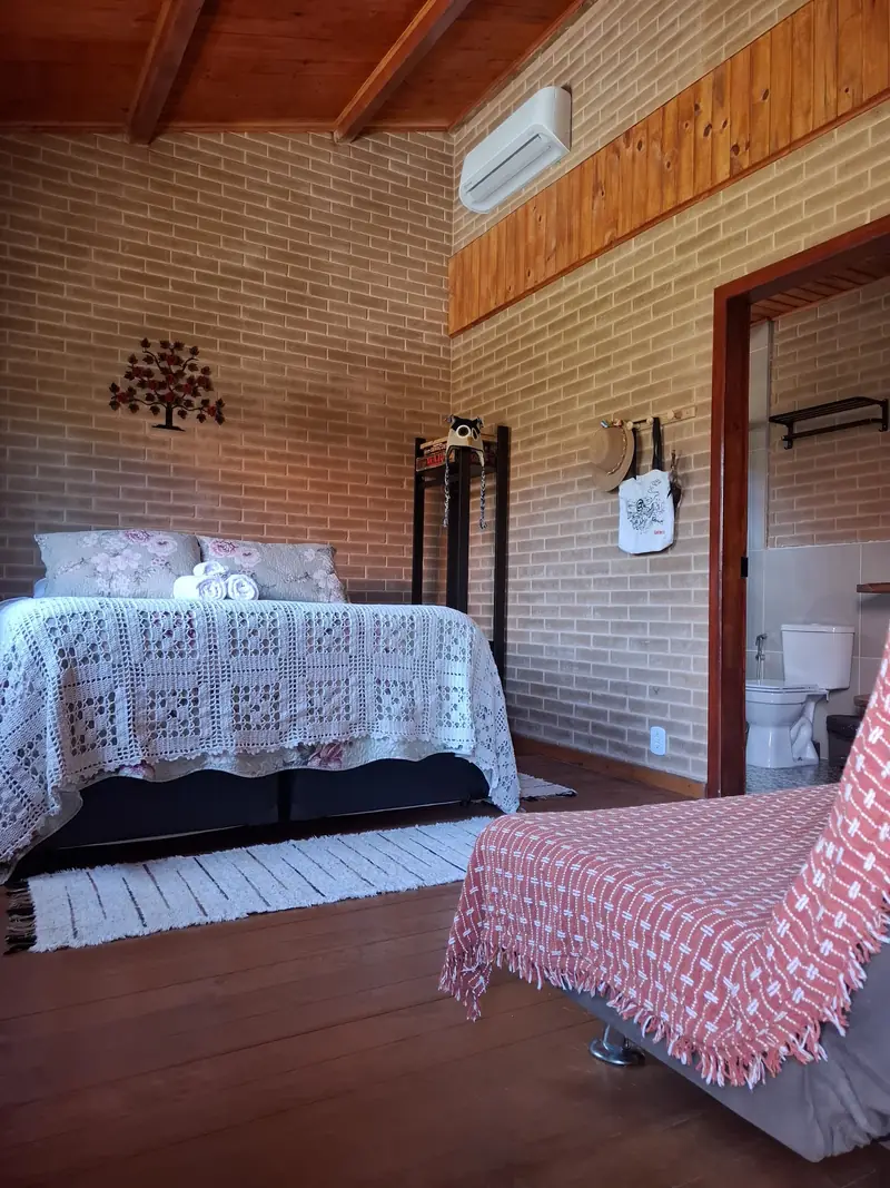 Interior da Cabana Lua com paredes de tijolo ecológico, cama de casal com decoração de artesanato regional e banheiro privativo